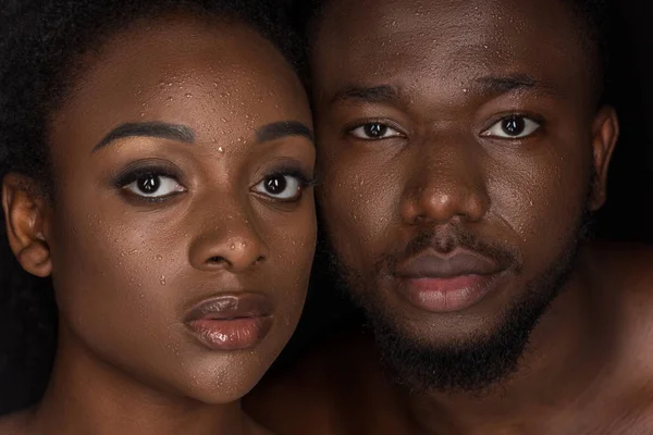 Jovem casal afro-americano com gotas de água em rostos olhando para a câmera em preto — Fotografia de Stock