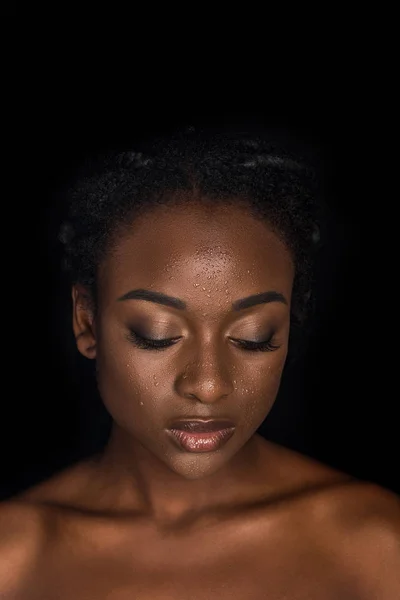 Retrato de sensual joven afroamericana con gotas de agua en la cara posando con los ojos cerrados aislados en negro - foto de stock