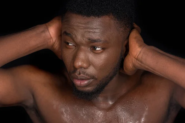 Young bare chested sweaty african american man closing ears with hands and looking away isolated on black — Stock Photo