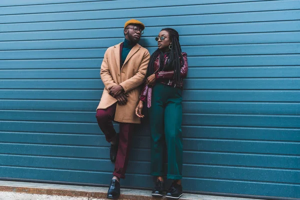 Vue pleine longueur de couple afro-américain élégant en veste et manteau posant ensemble sur la rue — Photo de stock