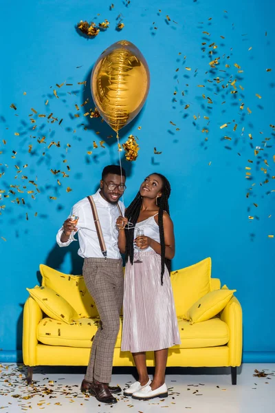 Feliz jovem casal afro-americano segurando copos de champanhe e balão dourado — Fotografia de Stock