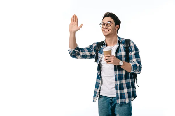 Bello studente in possesso di caffè in tazza di carta e mano ondulante isolato su bianco — Foto stock