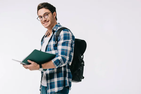 Smiling handsome student holding copybook and looking at camera isolated on white — Stock Photo