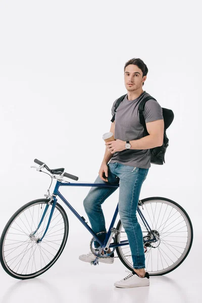 Гарний студент сидить на велосипеді і тримає каву, щоб йти на білому — стокове фото