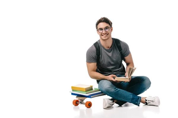 Étudiant beau et souriant assis sur le patin et tenant livre sur blanc — Photo de stock