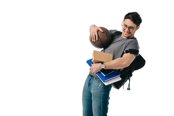 Спантеличений красивий студент тримає книги і баскетбол ізольовані на білому — стокове фото