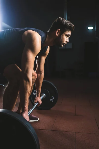 Vista laterale del giovane atleta che si prepara a sollevare il bilanciere in palestra — Foto stock