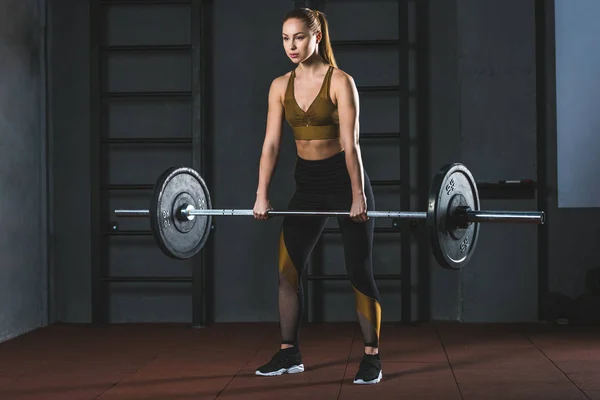 Front view of young sportswoman exercising with barbell in sports hall — Stock Photo
