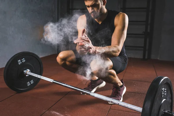 Giovane sportivo spargere polvere di gesso nelle mani per l'esercizio con bilanciere in palestra — Foto stock