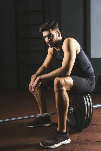 Young caucasian sportsman sitting on barbell in gym — Stock Photo