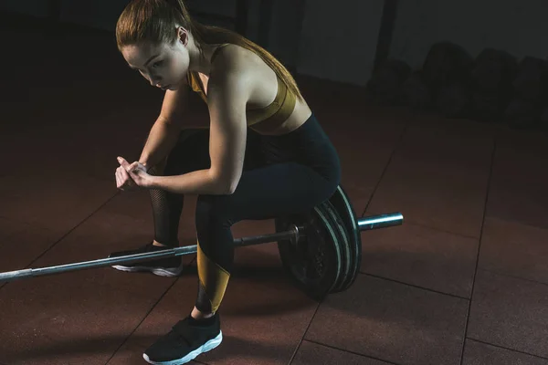 Frustrated young sportswoman sitting on barbell in gym — Stock Photo