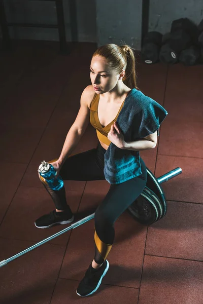 Blick aus der Vogelperspektive auf junge ruhende Sportlerin mit Handtuch und Flasche im Fitnessstudio — Stockfoto