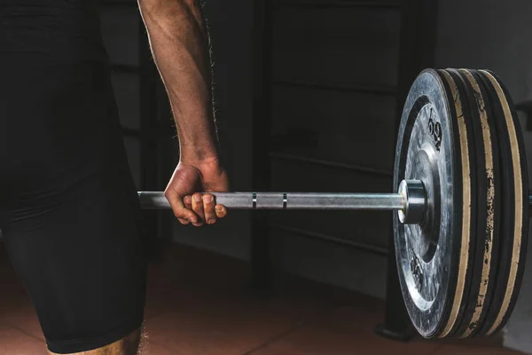 Cropped image of sportsman holding barbell in gym — Stock Photo