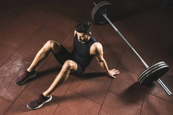 Vista de ángulo alto del deportista en reposo sentado cerca de la barra de pesas en el gimnasio — Stock Photo