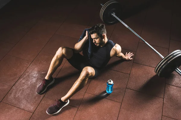 Vista de ángulo alto del deportista cansado limpiando cara por toalla en el gimnasio - foto de stock