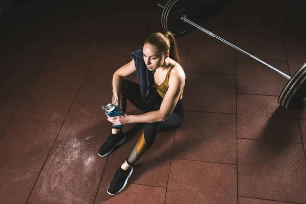 Hochwinkelblick auf ruhende Sportlerin mit Flasche und Handtuch im Fitnessstudio — Stockfoto
