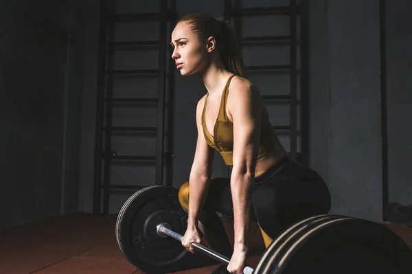 Side view of young bodybuilder preparing to raise barbell in gym — Stock Photo