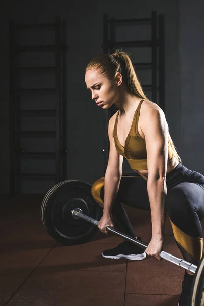 Young female bodybuilder preparing to raise barbell in gym — Stock Photo