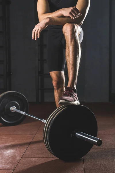 Cropped image of resting sportsman standing on barbell in gym — Stock Photo