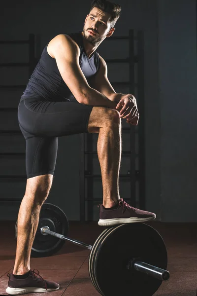 Jeune sportif au repos debout sur un haltère dans une salle de gym — Photo de stock