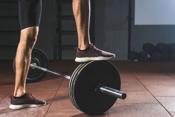 Cropped image of sportsman standing on barbell  in gym — Stock Photo