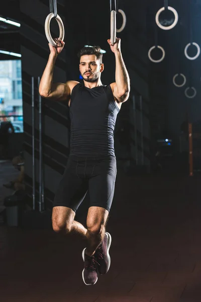 Young sportsman doing exercise on gymnastic rings in sports center — Stock Photo