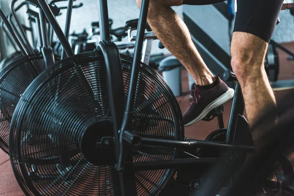 Imagen recortada del deportista haciendo ejercicio en bicicleta estática en el centro deportivo - foto de stock