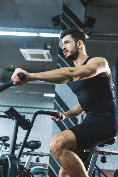 Vista a basso angolo dello sportivo che fa allenamento in cyclette nel centro sportivo — Foto stock