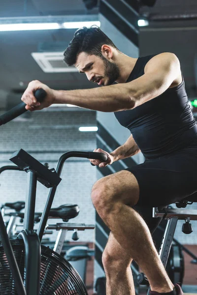 Jovem desportista fazendo treino em bicicleta de exercício no centro de esportes — Fotografia de Stock