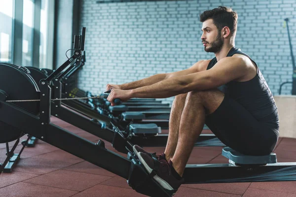 Joven deportista haciendo ejercicio sobre máquina de remo en el centro deportivo - foto de stock