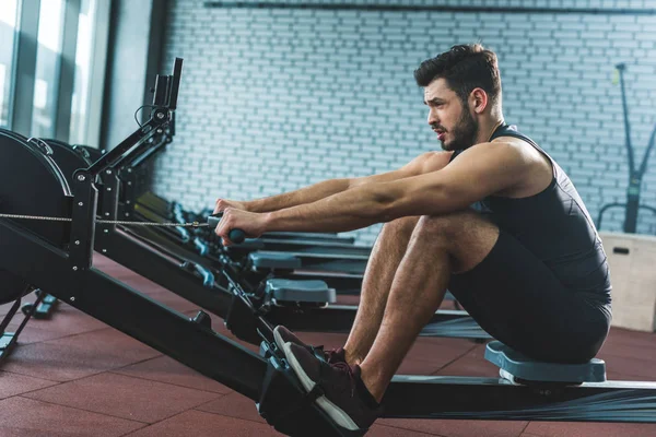 Vue latérale du sportif faisant de l'exercice sur une machine à ramer dans un centre sportif — Photo de stock