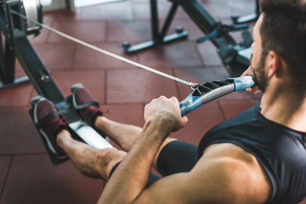 Cropped image of young sportsman doing exercise on rowing machine in sports center — Stock Photo