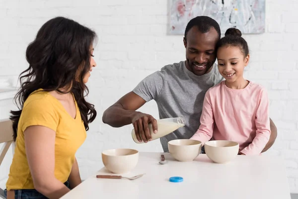 Beautiful young family pouring milk into cereal breakfast — Stock Photo