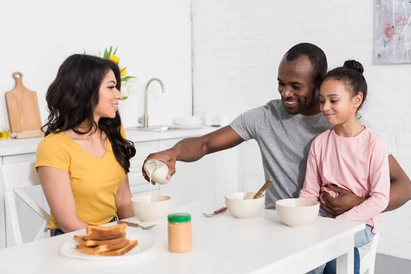 Família jovem feliz preparando café da manhã de cereais na cozinha juntos — Fotografia de Stock