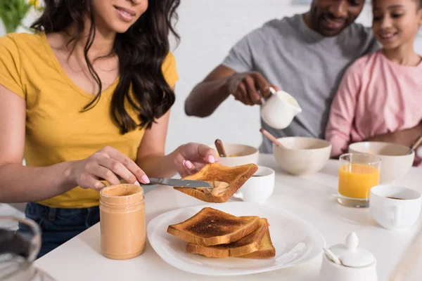 Cropped shot of woman applying peanut butter on toasts for husband and daughter — Stock Photo