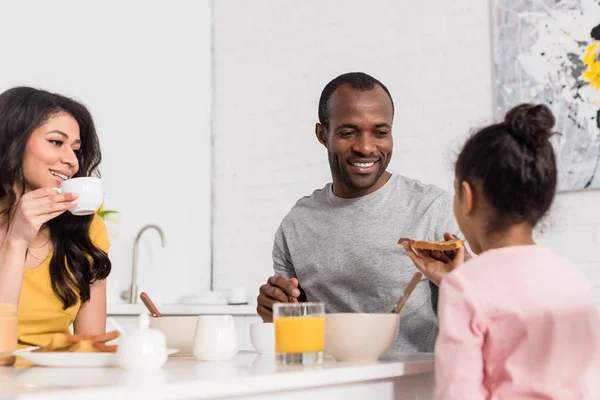 Sorrindo jovem família tomando café da manhã na cozinha juntos — Fotografia de Stock