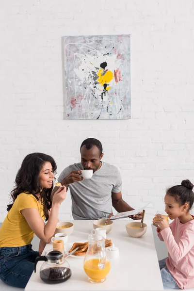 Feliz familia joven desayunando juntos en la cocina - foto de stock
