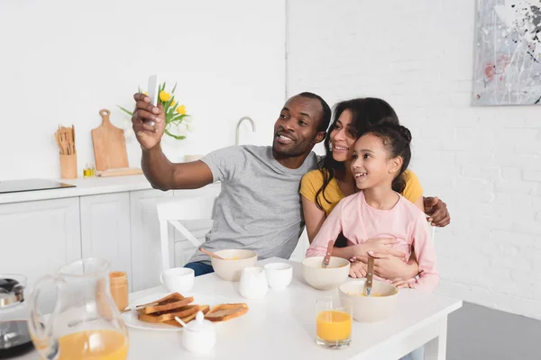 Feliz jovem família tomando selfie na cozinha enquanto toma café da manhã — Fotografia de Stock
