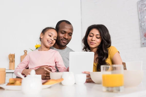 Familia joven feliz usando la tableta en la cocina mientras desayuna - foto de stock