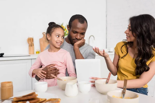 Jovem família usando tablet na cozinha enquanto toma café da manhã — Fotografia de Stock