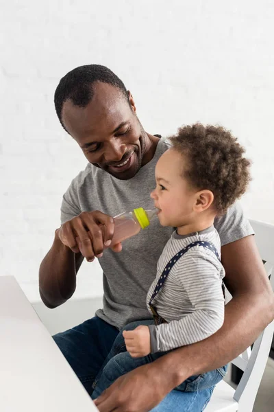 Father giving bottle of drink to his little son — Stock Photo