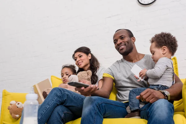 Feliz familia joven viendo la televisión juntos en el sofá - foto de stock