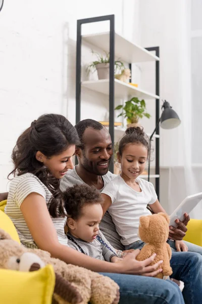 Feliz familia joven pasar tiempo junto con los dispositivos en el sofá acogedor — Stock Photo