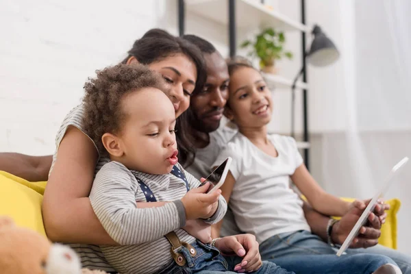 Glückliche junge Familie, die Zeit mit Geräten auf der Couch verbringt — Stockfoto