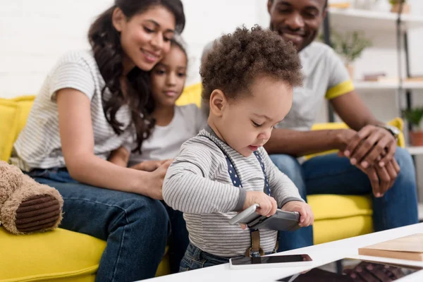 Glückliche junge Familie schaut Sohn beim Spielen mit Gadgets an — Stockfoto