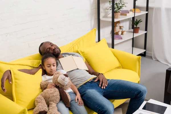 Padre e hija durmiendo juntos en el sofá después de leer cuento de hadas - foto de stock