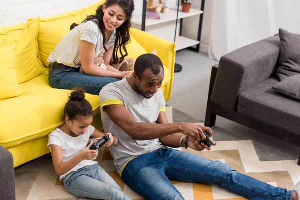 Excited father and daughter playing video games while mother sitting on couch — Stock Photo