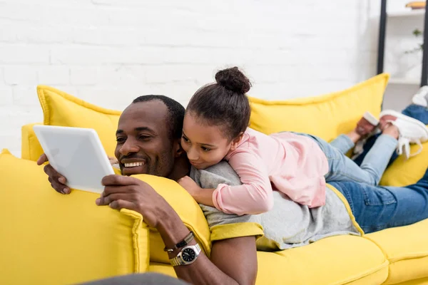 Père et fille couchés sur le canapé ensemble et en utilisant la tablette — Photo de stock