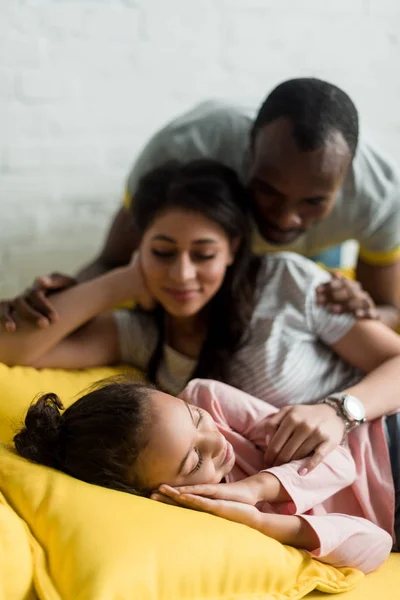 Padres jóvenes mirando a su hija durmiendo en el sofá - foto de stock