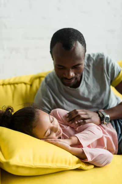 Отец смотрит на дочь, пока она спит на диване — стоковое фото